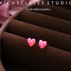 May include: A pair of heart-shaped earrings with a pink opal design. The earrings are displayed in a brown jewelry box. The text "MICHELLELEE STUDIO" and "Handcrafted Jewellery" are visible.