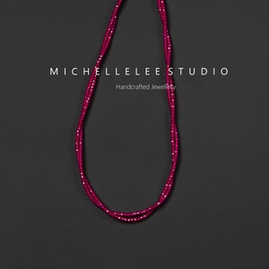 Könnte beinhalten: Eine zweireihige Halskette aus kleinen, rosafarbenen Perlen. Die Halskette hat einen silbernen Verschluss und wird vor einem schwarzen Hintergrund präsentiert. Der Text "MICHELLELEE STUDIO Handgefertigter Schmuck" ist unterhalb der Halskette sichtbar.