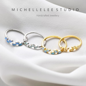 May include: Four rings featuring a leaf-inspired design with small, iridescent blue and white stones. Two rings are silver-toned and two are gold-toned. The text MICHELLELEE STUDIO Handcrafted Jewellery is visible at the top of the image.