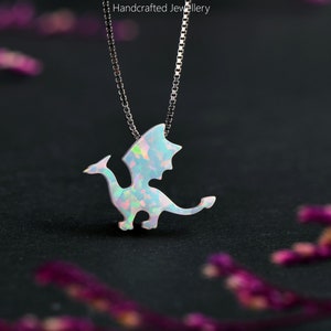 May include: A silver necklace with a dragon pendant. The pendant is white with iridescent accents, and the chain is a delicate silver. The background is dark, with the text "MICHELLELEEESTUDIO Handcrafted Jewellery".