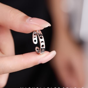 May include: A silver ring with a crescent moon design. The open, adjustable ring features a series of crescent moon cutouts. The ring is held between fingers against a blurred background. The text "MICHELLELEE STUDIO" and "Handcrafted Jewellery" are visible.