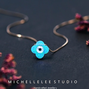 May include: A delicate silver chain necklace with a blue opal flower pendant featuring a white evil eye charm. The necklace is handcrafted and is a popular symbol of protection and good luck.