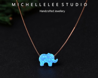 May include: A delicate necklace featuring a small, light blue elephant pendant. The pendant is made of a shimmering material and hangs from a thin, rose-gold colored chain. The text "MICHELLELEE STUDIO Handcrafted Jewellery" is visible.