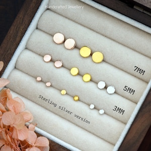 May include: A wooden box with a variety of small, round, silver, gold, and rose gold earrings. The earrings are arranged in rows by size, with the largest earrings at the top and the smallest earrings at the bottom. The box is labeled "Michelle Lee Studio" and "Handcrafted Jewellery". The earrings are available in 3mm, 5mm, and 7mm sizes.