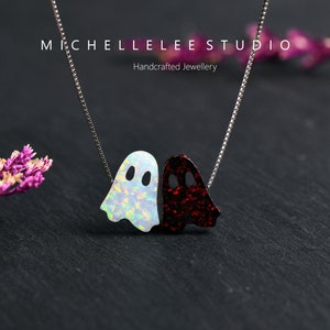 May include: A silver chain necklace with a white and red opal ghost charm. The charm is made of two ghosts, one white and one red, that are facing each other. The necklace is handcrafted and is perfect for Halloween.