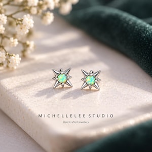 Op de afbeelding: Een paar zilverkleurige oorknopjes met een centrale ronde iriserende opaalsteen, omringd door een vierpuntige sterrenvormige omlijsting. De tekst MICHELLELEE STUDIO Handcrafted Jewellery staat onder de oorbellen op het oppervlak gedrukt.