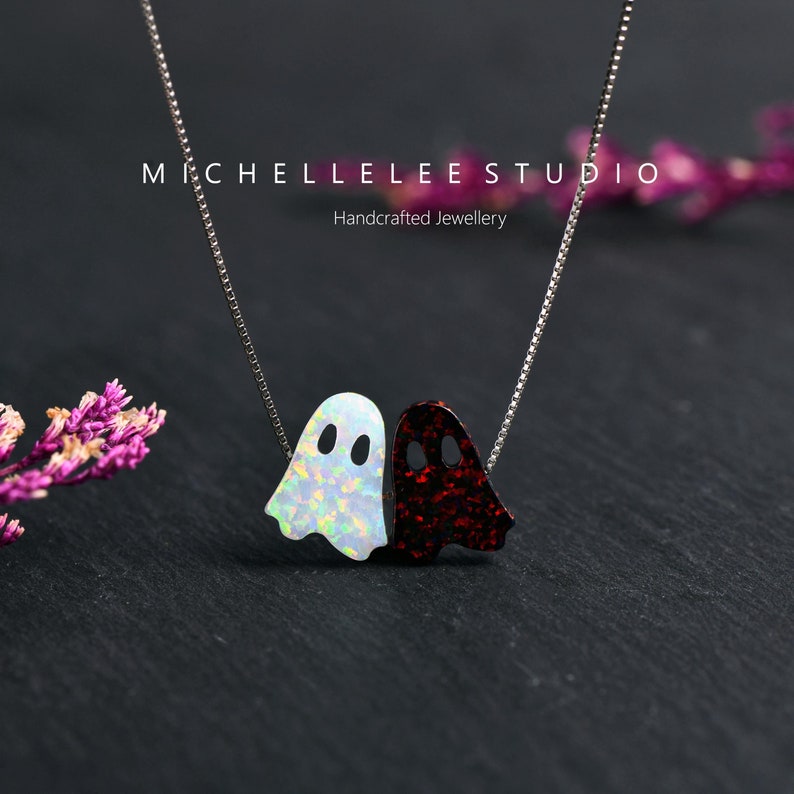 May include: A silver chain necklace with a white and red opal ghost charm. The charm is made of two ghosts, one white and one red, that are facing each other. The necklace is handcrafted and is perfect for Halloween.