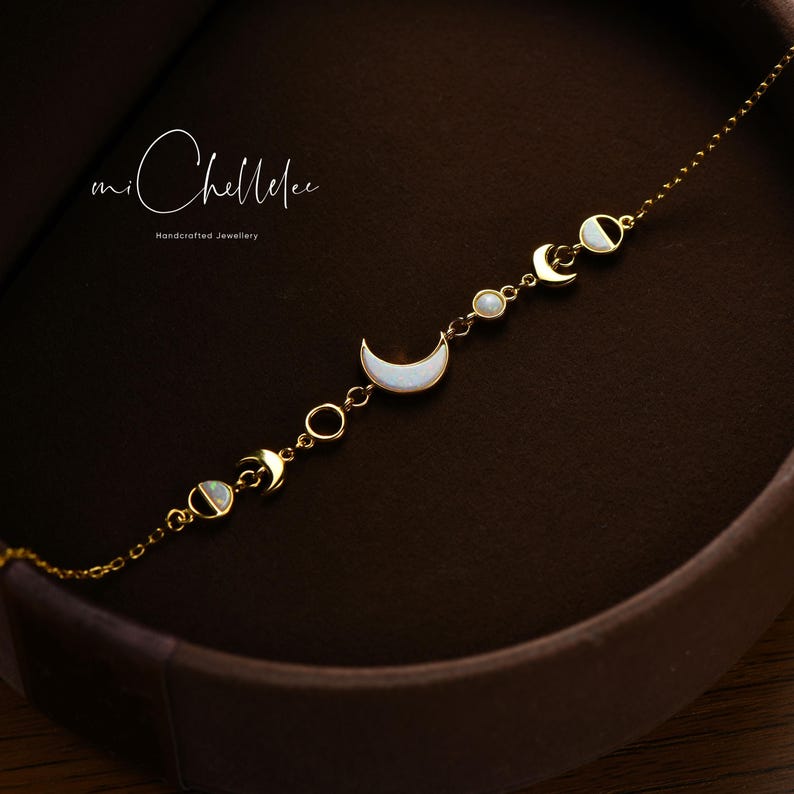 May include: A delicate gold-toned bracelet featuring moon phase charms with white mother-of-pearl inlays. The bracelet includes crescent moons, circles, and round accents. The image also shows the text "mi Chellelee Handcrafted Jewellery".