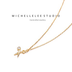 May include: A gold chain necklace with a small gold pendant shaped like a pair of scissors with a single clear gemstone in the center.