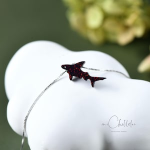 May include: A silver chain necklace with a red glitter shark pendant. The pendant is made of resin and has a sparkly finish. The necklace is a great gift for anyone who loves sharks or the ocean.