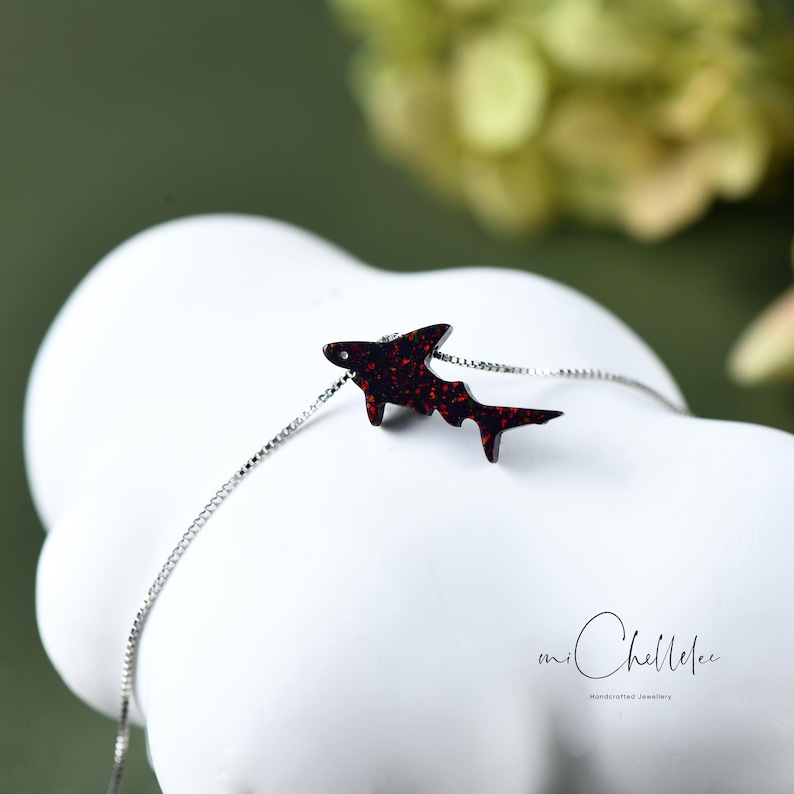 May include: A silver chain necklace with a red glitter shark pendant. The pendant is made of resin and has a sparkly finish. The necklace is a great gift for anyone who loves sharks or the ocean.