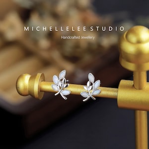 Pode incluir: Um par de brincos de prata com um delicado design de ramo adornado com pedras de opala branca. Os brincos são exibidos em um suporte dourado. Michellelee Studio Joias artesanais.