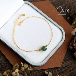 May include: A gold chain bracelet with a green jade bead. The bracelet is in a white box with the text "mi Chelle Jewelry" on the side.