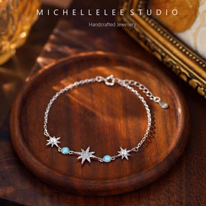 May include: A silver bracelet with star and turquoise accents. The bracelet features a delicate chain with alternating star-shaped charms and small turquoise-colored stones. The image includes the text "MICHELLELEE STUDIO Handcrafted Jewellery".