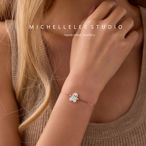 Pu&ograve; includere: Un delicato bracciale a catena in oro rosa con un piccolo ciondolo bianco a forma di fantasma. Il testo MICHELLELEE STUDIO Handcrafted Jewellery &egrave; visibile nella parte superiore dell'immagine. Il bracciale ha una catena sottile e regolabile.