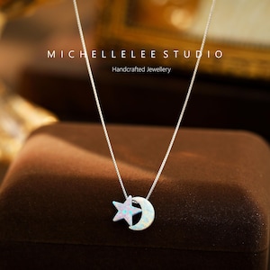 May include: A silver chain necklace with a star and crescent moon pendant made of white opal. The pendant is on a brown velvet surface. The text "MICHELLELEE STUDIO Handcrafted Jewellery" is visible above the pendant.