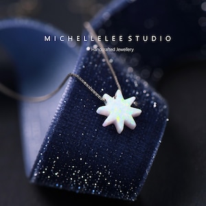 Op de afbeelding: Een zilveren ketting met een witte opaal ster hanger. De ketting wordt gepresenteerd in een blauwe fluwelen doos. De tekst "MICHELLELEE STUDIO" en "Handgemaakt juweel" is zichtbaar op de doos.