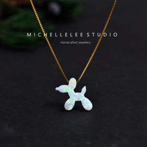 May include: A gold chain necklace with a pendant shaped like a balloon dog. The pendant is white with iridescent flecks. The text "MICHELLELEE STUDIO Handcrafted Jewellery" is above the necklace.