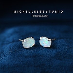 May include: A pair of silver stud earrings with oval-shaped white opal gemstones. The earrings are set against a blue velvet background.