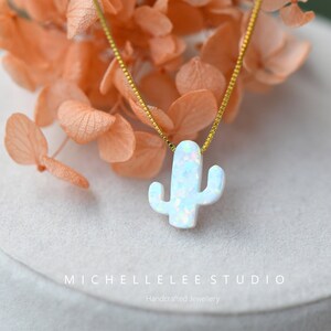 Op de afbeelding: Een delicate gouden ketting met een witte opaal cactus hanger. De hanger is een eenvoudig, minimalistisch ontwerp met een kleine, delicate cactusvorm.