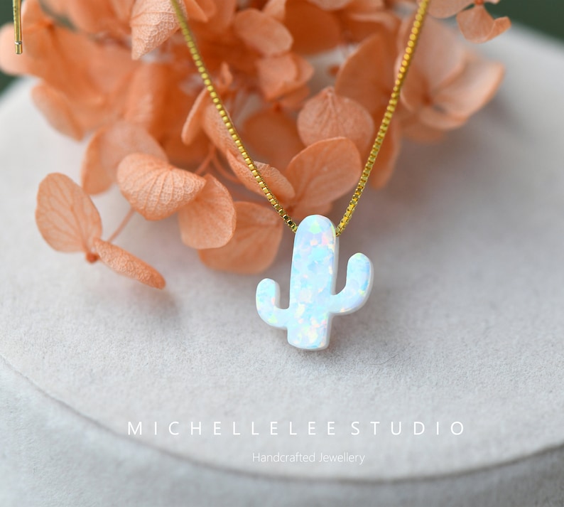 Op de afbeelding: Een delicate gouden ketting met een witte opaal cactus hanger. De hanger is een eenvoudig, minimalistisch ontwerp met een kleine, delicate cactusvorm.