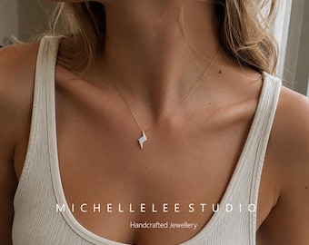 May include: A delicate gold chain necklace featuring a small, silver-toned lightning bolt pendant. The text MICHELLELEE STUDIO Handcrafted Jewellery is visible at the bottom of the image. The necklace is worn against a white ribbed tank top.