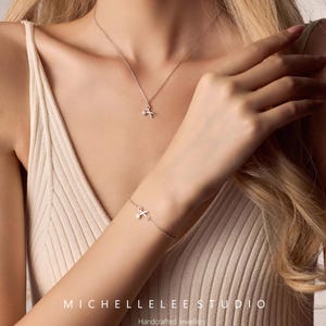 May include: A silver necklace and bracelet with a delicate cross pendant. The jewelry is handcrafted and features a small, sparkling stone in the center of the cross.