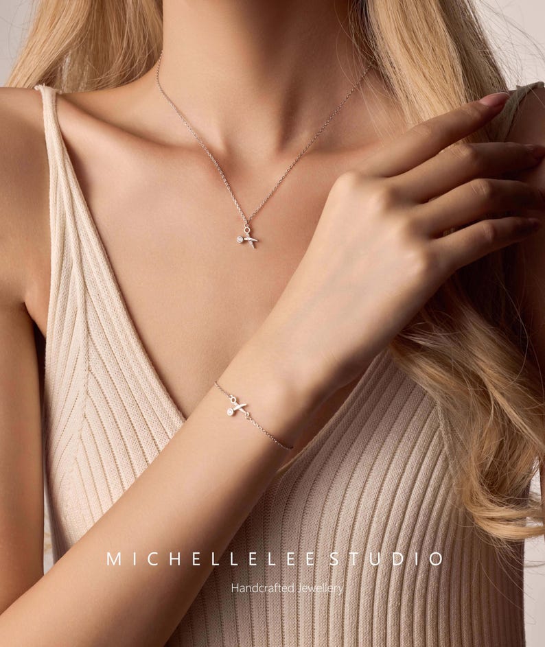 May include: A silver necklace and bracelet with a delicate cross pendant. The jewelry is handcrafted and features a small, sparkling stone in the center of the cross.