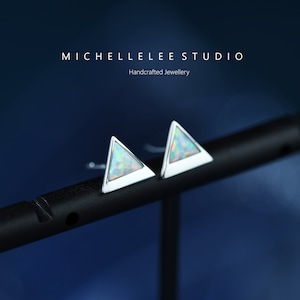 May include: A pair of silver triangle earrings with iridescent opal stones. The earrings are on a black display stand. MICHELLELEESTUDIO Handcrafted Jewellery.