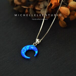 May include: A silver chain necklace with a crescent moon pendant made of blue opal. The pendant is set in silver and has a delicate, feminine design.