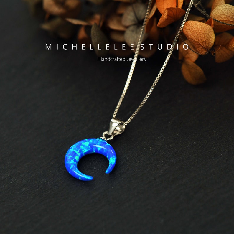 May include: A silver chain necklace with a crescent moon pendant made of blue opal. The pendant is set in silver and has a delicate, feminine design.