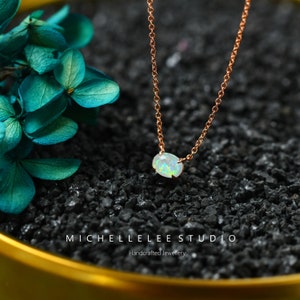 Könnte beinhalten: Eine zarte Halskette aus roségoldener Kette mit einem kleinen ovalen Opal-Anhänger. Der Opal hat eine milchig weiße Basis mit grün- und blaufarbenen Schimmern.