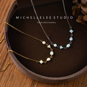May include: Two delicate necklaces with opal stones in geometric shapes. The necklaces are on a brown background with the text "MICHELLE LEE STUDIO Handcrafted Jewellery".