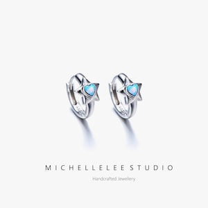 May include: Two silver hoop earrings, each with a star-shaped design and a light blue heart-shaped opal centre. The text "MICHELLELEE STUDIO" and "Handcrafted Jewellery" are at the bottom of the image.