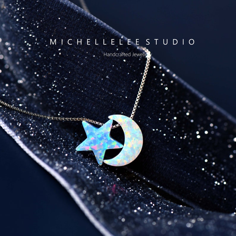 May include: A silver chain necklace with a crescent moon and star pendant made of iridescent opal. The pendant is on a black velvet background.  Handcrafted Jewellery by Michelle Lee Studio.