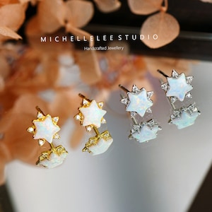 May include: A pair of star-shaped stud earrings with a white opal center and small clear crystals. The earrings are available in gold and silver tones. The text "MICHELLE LEE STUDIO Handcrafted Jewellery" is visible.