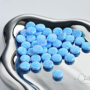 May include: A pile of light blue opal cabochons, each with a unique iridescent pattern, are displayed on a silver tray.