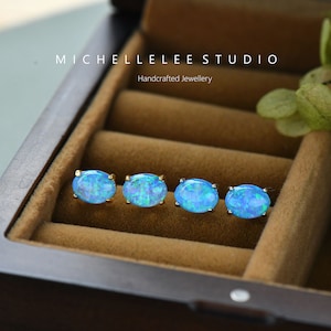 May include: Four pairs of oval-shaped blue opal earrings in a jewelry box. The earrings are set in gold and have a delicate design. The box is made of wood and has a velvet lining.