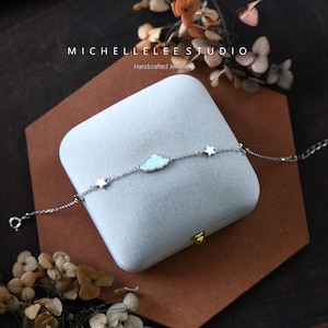 May include: A silver bracelet with a cloud charm and star charms. The bracelet is in a light blue velvet box. The box has the text "MICHELLELEE STUDIO Handcrafted Jewellery" on the top.