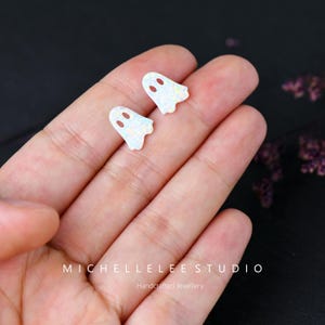 May include: A pair of white opal ghost earrings. The earrings are small and have a sparkly finish.