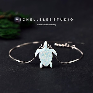 Op de afbeelding: Een zilveren armband met een witte opaal schildpad hanger. De hanger heeft een getextureerd oppervlak en is verbonden met een fijne ketting. De tekst "MICHELLELEE STUDIO" en "Handcrafted Jewellery" is ook zichtbaar.