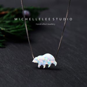 May include: A silver chain necklace with a white opal bear pendant. The bear is facing right and has a detailed design. The necklace is on a dark background.