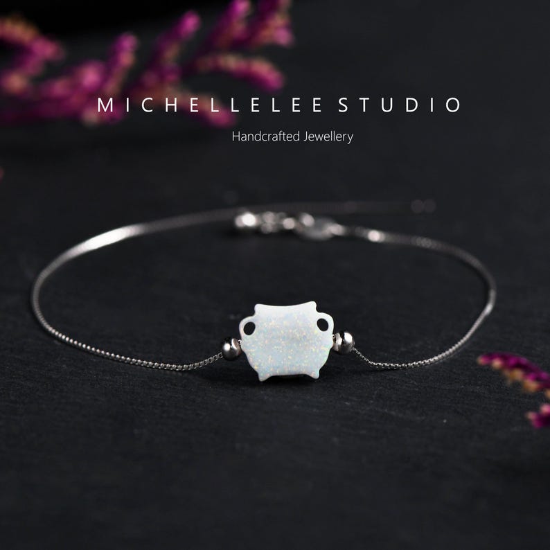 May include: A delicate silver chain bracelet with a white opal charm in the shape of a small pot. The bracelet is on a black background.  MICHELLELEE STUDIO Handcrafted Jewellery