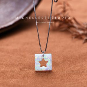 May include: A silver chain necklace with a square pendant featuring a white opal with a star cut-out. The pendant is set against a brown background. The text "MICHELLELEESTUDIO Handcrafted Jewellery" is visible above the pendant.