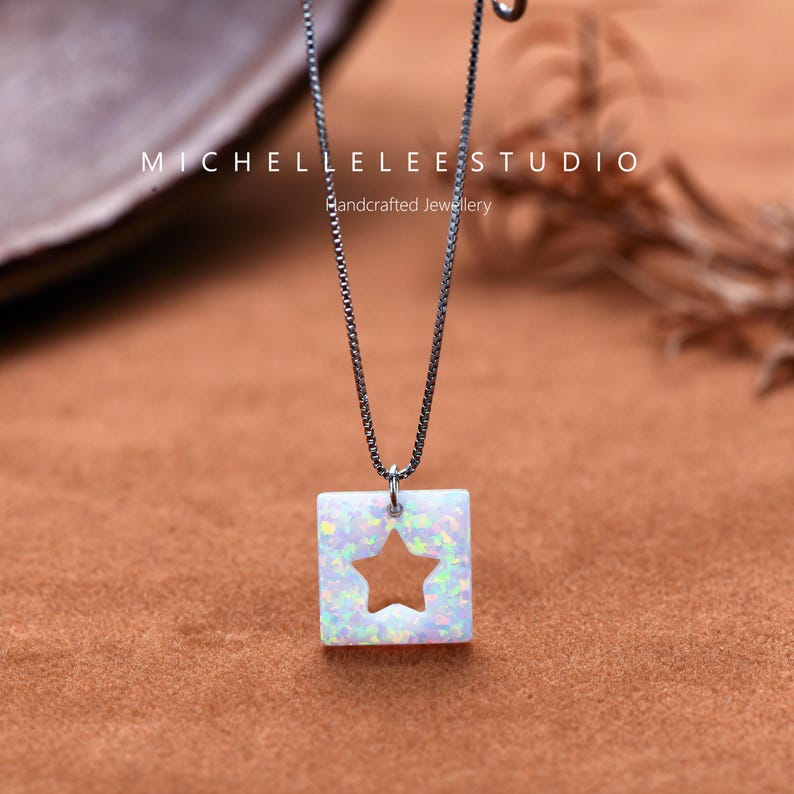 May include: A silver chain necklace with a square pendant featuring a white opal with a star cut-out. The pendant is set against a brown background. The text "MICHELLELEESTUDIO Handcrafted Jewellery" is visible above the pendant.