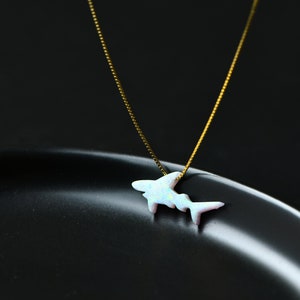 May include: A delicate gold chain necklace with a white opal shark pendant. The pendant is a simple silhouette of a shark with a shimmering opal finish. The necklace is on a black background with the text "MICHELLELEE STUDIO Handcrafted Jewellery".