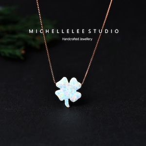 May include: A necklace with a four-leaf clover pendant. The pendant is white with iridescent flecks, hanging from a fine, rose-gold chain. The text "MICHELLELEE STUDIO Handcrafted Jewellery" is at the top.