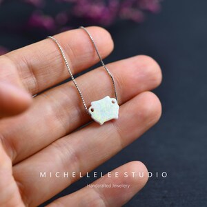 May include: A delicate silver chain necklace with a white opal pendant in the shape of a small pot. The pendant has a textured surface and is accented with small silver details.