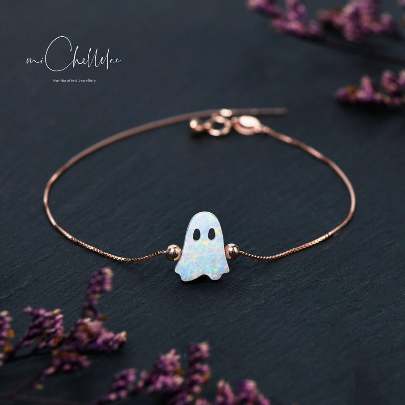 May include: A delicate rose gold chain bracelet with a white opal ghost charm. The charm has two small black eyes.