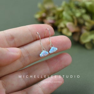 Peut inclure: Une paire de boucles d'oreilles pendantes en argent avec une pierre d'opale en forme de nuage. Les boucles d'oreilles sont délicates et féminines.